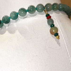 Puede incluir: Un collar de piedras preciosas verdes con un cierre de oro y un borla de cuentas multicolores.