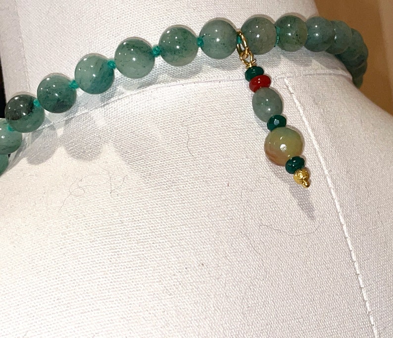 Puede incluir: Un collar de piedras preciosas verdes con un cierre de oro y un borla de cuentas multicolores.