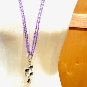 May include: A long, layered necklace made of light purple beads with a silver pendant featuring multiple amethyst stones.