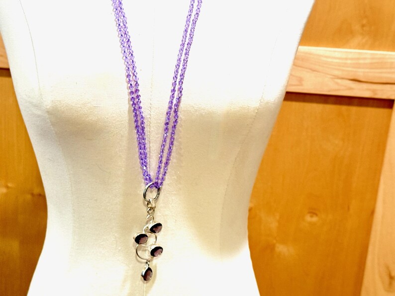 May include: A long, layered necklace made of light purple beads with a silver pendant featuring multiple amethyst stones.