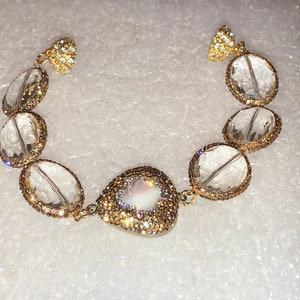 May include: A gold bracelet with clear crystal beads and a pearlescent heart-shaped charm.