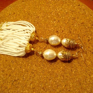 May include: A pair of gold earrings with white pearl beads and white beaded tassels.