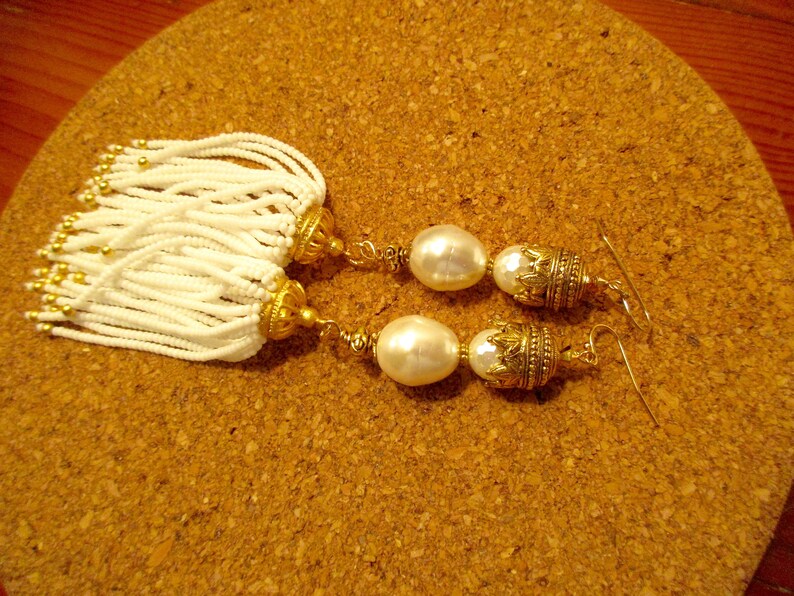 May include: A pair of gold earrings with white pearl beads and white beaded tassels.