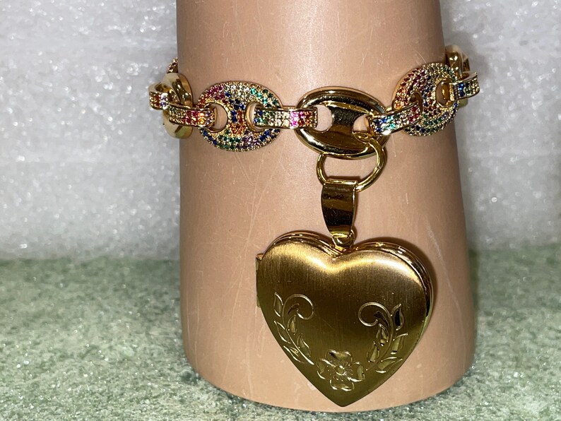 May include: A gold chain bracelet with a rainbow of colorful stones and a gold heart-shaped locket pendant.