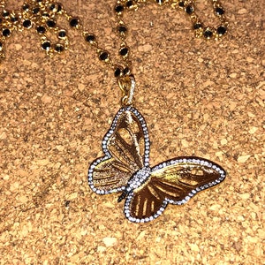 May include: A gold butterfly pendant necklace with clear rhinestones. The necklace has a black bead chain.