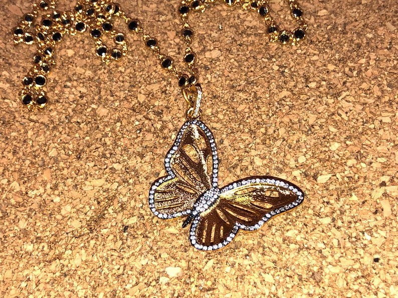 May include: A gold butterfly pendant necklace with clear rhinestones. The necklace has a black bead chain.