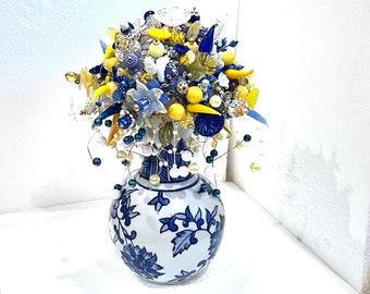 May include: A blue and white porcelain vase with a floral design, filled with a bouquet of yellow, blue, and white beads and other decorative elements.