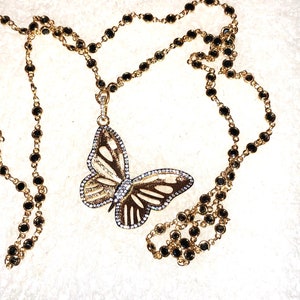 May include: A gold chain necklace with black beads and a butterfly pendant. The butterfly is made of gold and has clear stones on its wings.