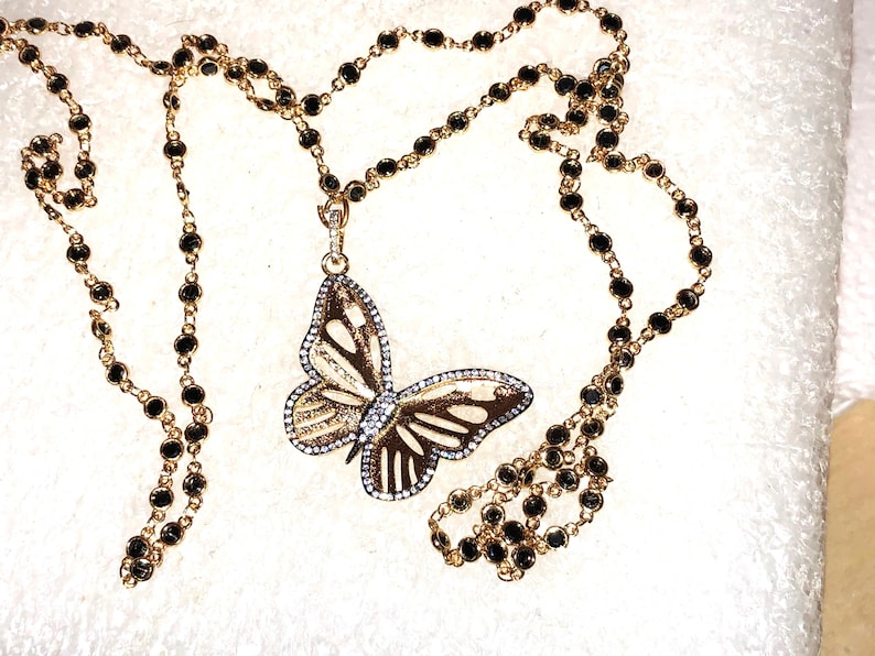 May include: A gold chain necklace with black beads and a butterfly pendant. The butterfly is made of gold and has clear stones on its wings.