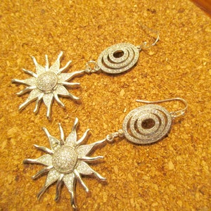 May include: A pair of silver earrings with a sunburst design and a circle design. The sunburst earrings have clear crystals and the circle earrings have a triple circle design with clear crystals.