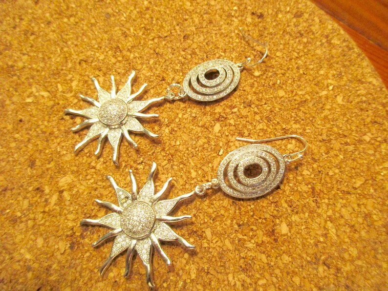 May include: A pair of silver earrings with a sunburst design and a circle design. The sunburst earrings have clear crystals and the circle earrings have a triple circle design with clear crystals.