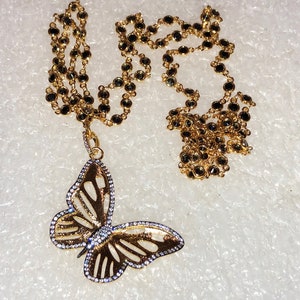 May include: A gold chain necklace with black beads and a gold butterfly pendant with clear stones.