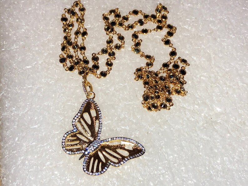 May include: A gold chain necklace with black beads and a gold butterfly pendant with clear stones.