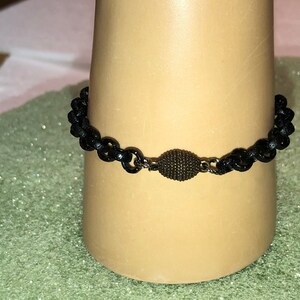 May include: A black chain bracelet with a small, round, dark brown bead in the center.