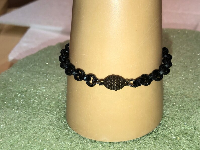May include: A black chain bracelet with a small, round, dark brown bead in the center.