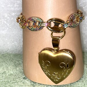 May include: A gold chain bracelet with a rainbow of colorful stones and a gold heart-shaped locket with an engraved floral design.