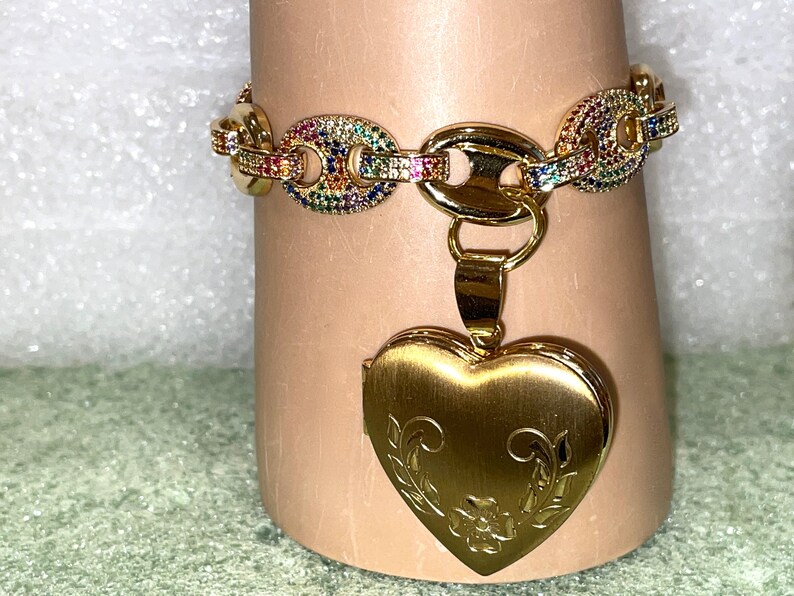 May include: A gold chain bracelet with a rainbow of colorful stones and a gold heart-shaped locket with an engraved floral design.