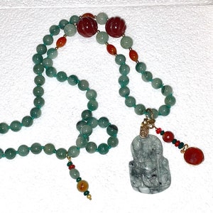 Puede incluir: Un collar de cuentas de jade verde con un colgante de jade con una figura tallada. El collar tambi&eacute;n incluye cuentas rojas y naranjas.