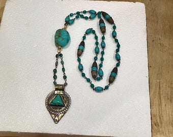 May include: A long turquoise and gold necklace with a large turquoise pendant. The pendant is a triangular shape with intricate details.