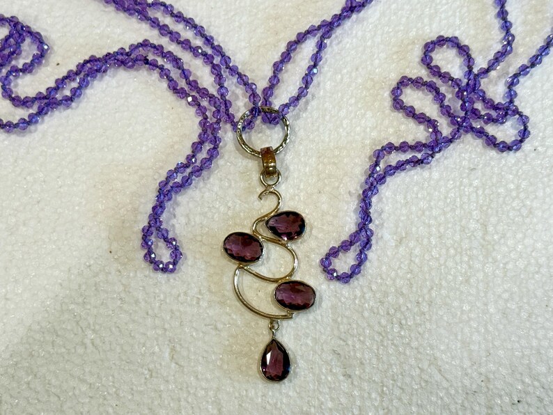 May include: A purple amethyst gemstone necklace with a pendant featuring a silver design with multiple amethyst stones. The necklace is made of multiple strands of small purple beads.