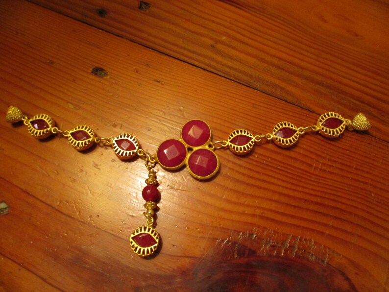 May include: A gold necklace with a pendant featuring a cluster of four red gemstones. The necklace is adorned with smaller red gemstones throughout.