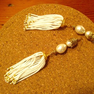 May include: A pair of white beaded tassel earrings with gold accents and pearl drops.