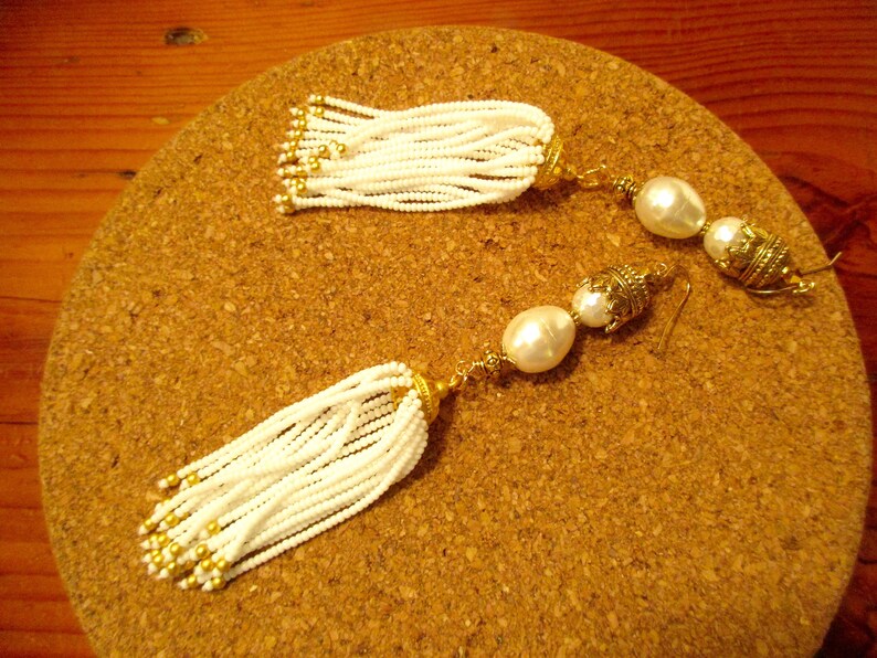 May include: A pair of white beaded tassel earrings with gold accents and pearl drops.