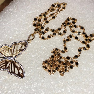 May include: A gold chain necklace with black beads and a gold butterfly pendant with clear rhinestones.