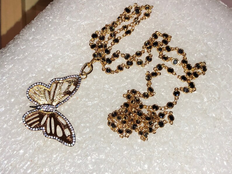 May include: A gold chain necklace with black beads and a gold butterfly pendant with clear rhinestones.