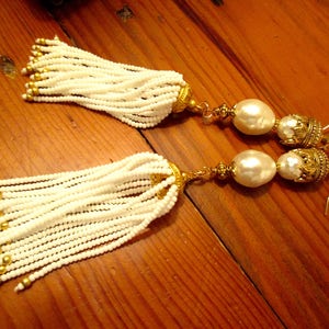 May include: A pair of white beaded tassel earrings with gold accents and large white pearl drops.