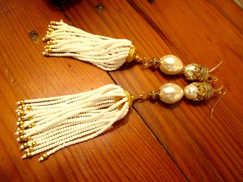 May include: A pair of white beaded tassel earrings with gold accents and large white pearl drops.