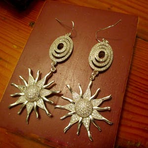 May include: A pair of silver earrings with a sunburst design and a circular pendant with clear rhinestones.