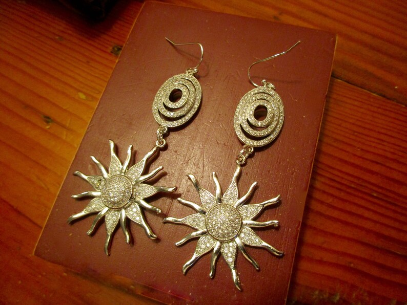 May include: A pair of silver earrings with a sunburst design and a circular pendant with clear rhinestones.