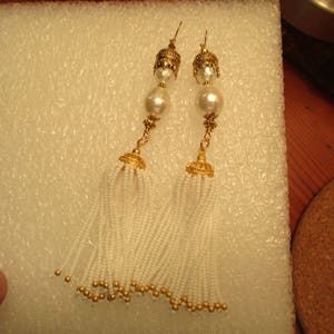 May include: A pair of gold tone earrings with white pearl accents and white beaded tassels.