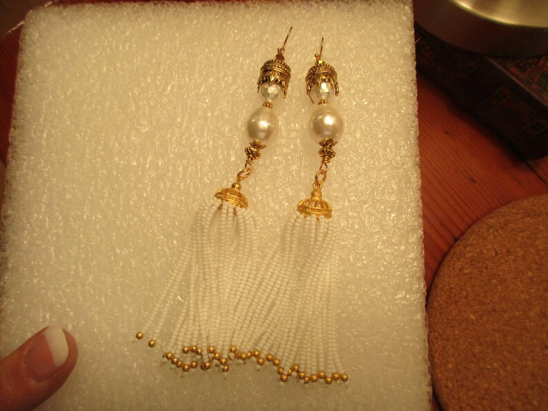 May include: A pair of gold tone earrings with white pearl accents and white beaded tassels.