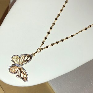 May include: A gold chain necklace with a black bead design and a butterfly pendant with clear stones.
