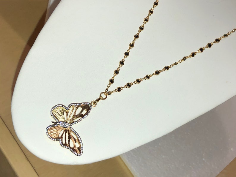 May include: A gold chain necklace with a black bead design and a butterfly pendant with clear stones.