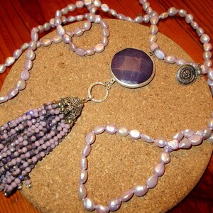 May include: A long lavender pearl necklace with a silver tassel and a large purple gemstone pendant.