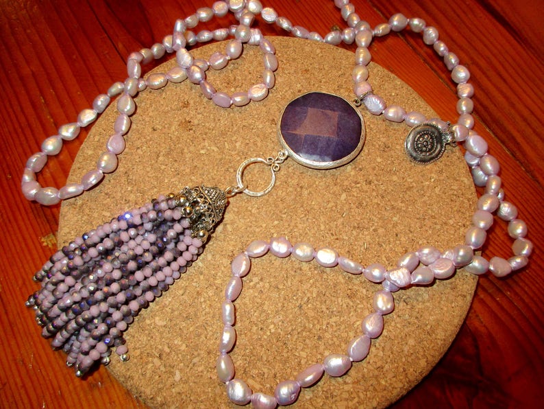 May include: A long lavender pearl necklace with a silver tassel and a large purple gemstone pendant.