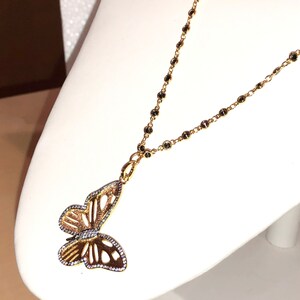 May include: A gold chain necklace with a black bead design and a delicate butterfly pendant. The butterfly is made of gold and has a clear crystal design.