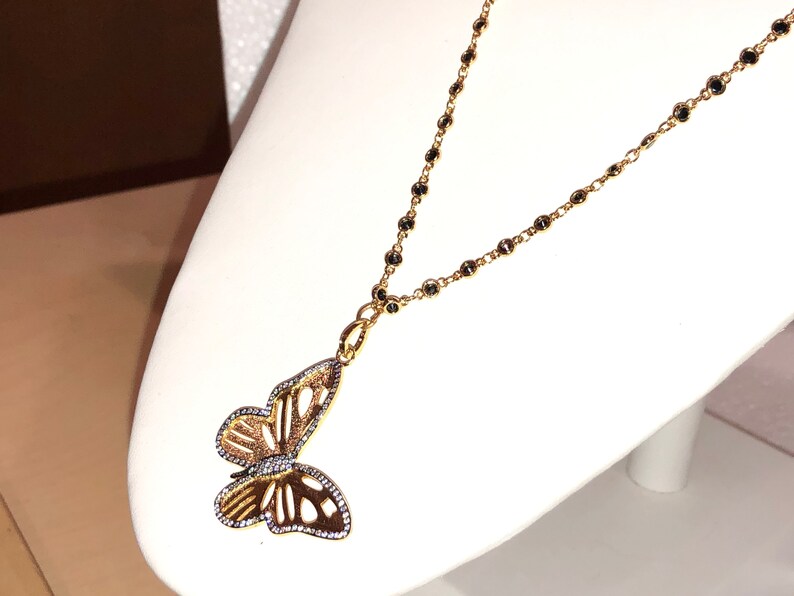 May include: A gold chain necklace with a black bead design and a delicate butterfly pendant. The butterfly is made of gold and has a clear crystal design.