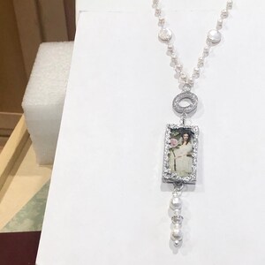 Pu&ograve; includere: Una collana d'argento con un ciondolo rettangolare che presenta un ritratto vintage di una donna. Il ciondolo &egrave; circondato da piccole pietre trasparenti. La collana &egrave; realizzata con perle bianche e argento.