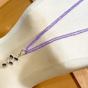 May include: A multi-strand necklace with a pendant made of multiple amethyst stones in a spiral design. The necklace is made of small, light purple beads.