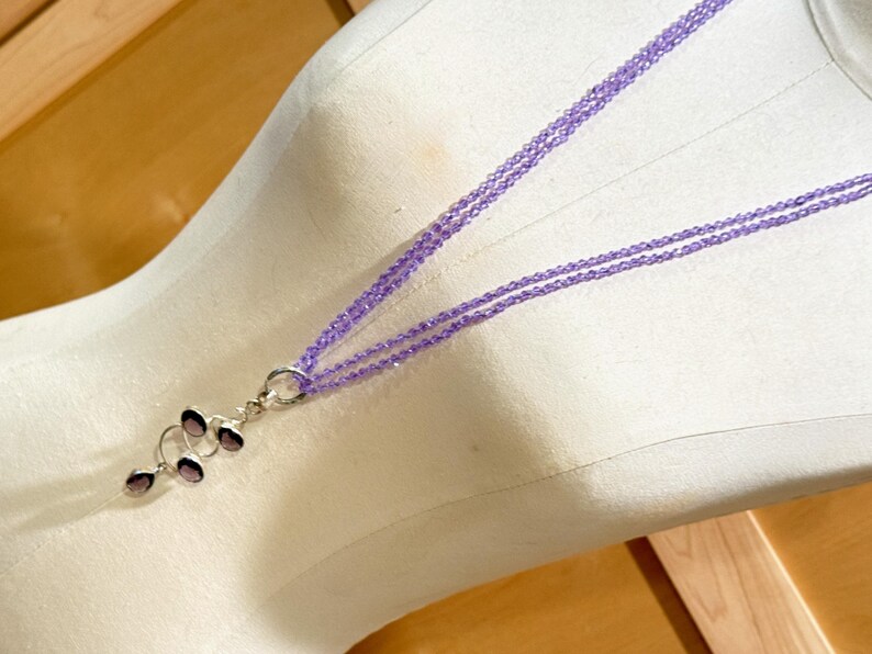 May include: A multi-strand necklace with a pendant made of multiple amethyst stones in a spiral design. The necklace is made of small, light purple beads.