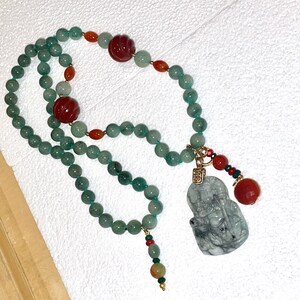 Puede incluir: Un collar de jade verde con cuentas rojas y naranjas y un colgante de jade con una figura tallada.