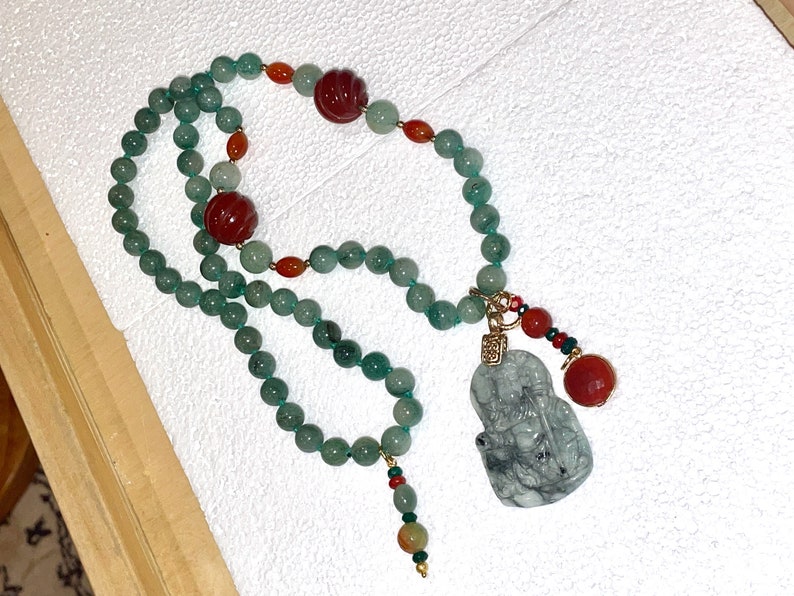 Puede incluir: Un collar de jade verde con cuentas rojas y naranjas y un colgante de jade con una figura tallada.