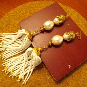 May include: A pair of white beaded tassel earrings with gold accents and large white pearl drops.