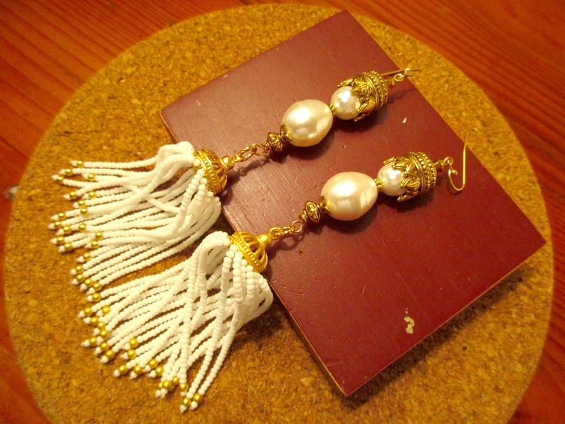 May include: A pair of white beaded tassel earrings with gold accents and large white pearl drops.