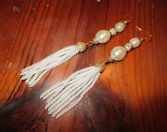 May include: A pair of white pearl tassel earrings with gold accents. The earrings feature a large white pearl and a tassel made of small white beads.