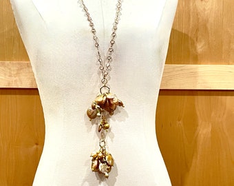 May include: A long silver chain necklace with two clusters of brown and gold iridescent pearls hanging from it.